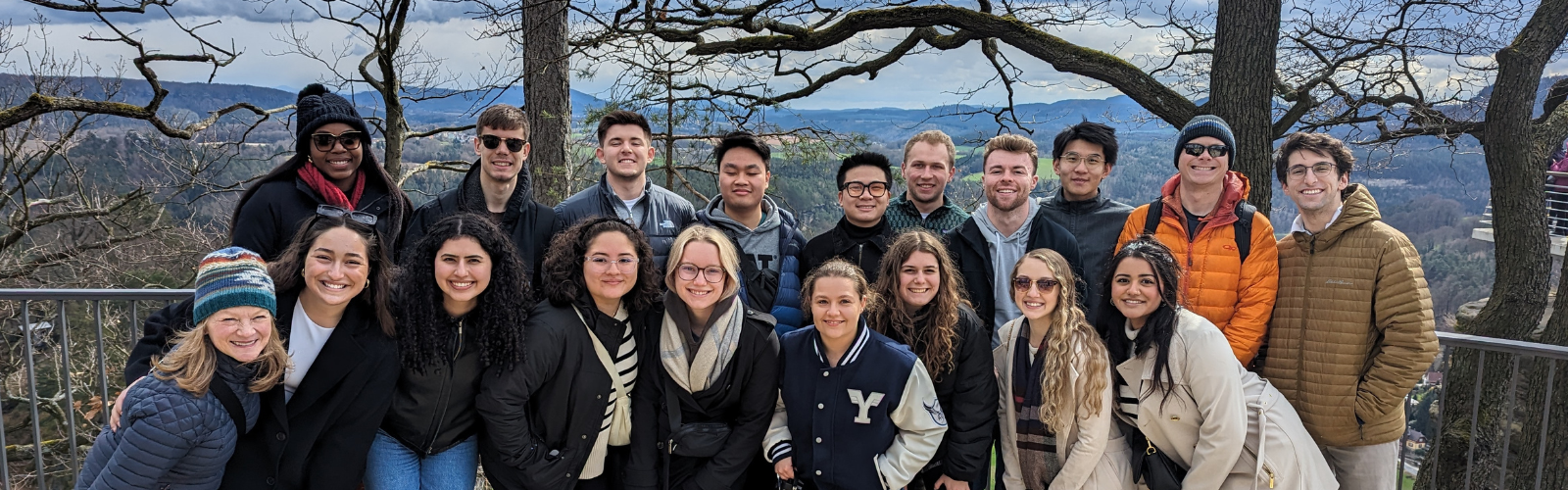 Students are gathered at a hilltop photo point. They are bundled in winter gear and smiling at the camera.